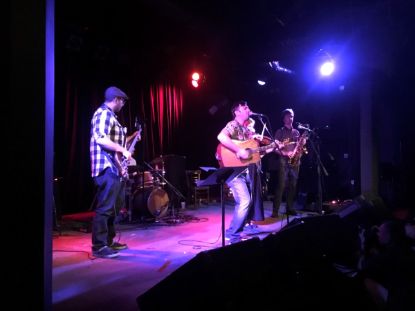 Phil C-B playing with the band Pet Peeve in Chicago in 2022. Dark photo with blue, red, and purple light cast across the stage.